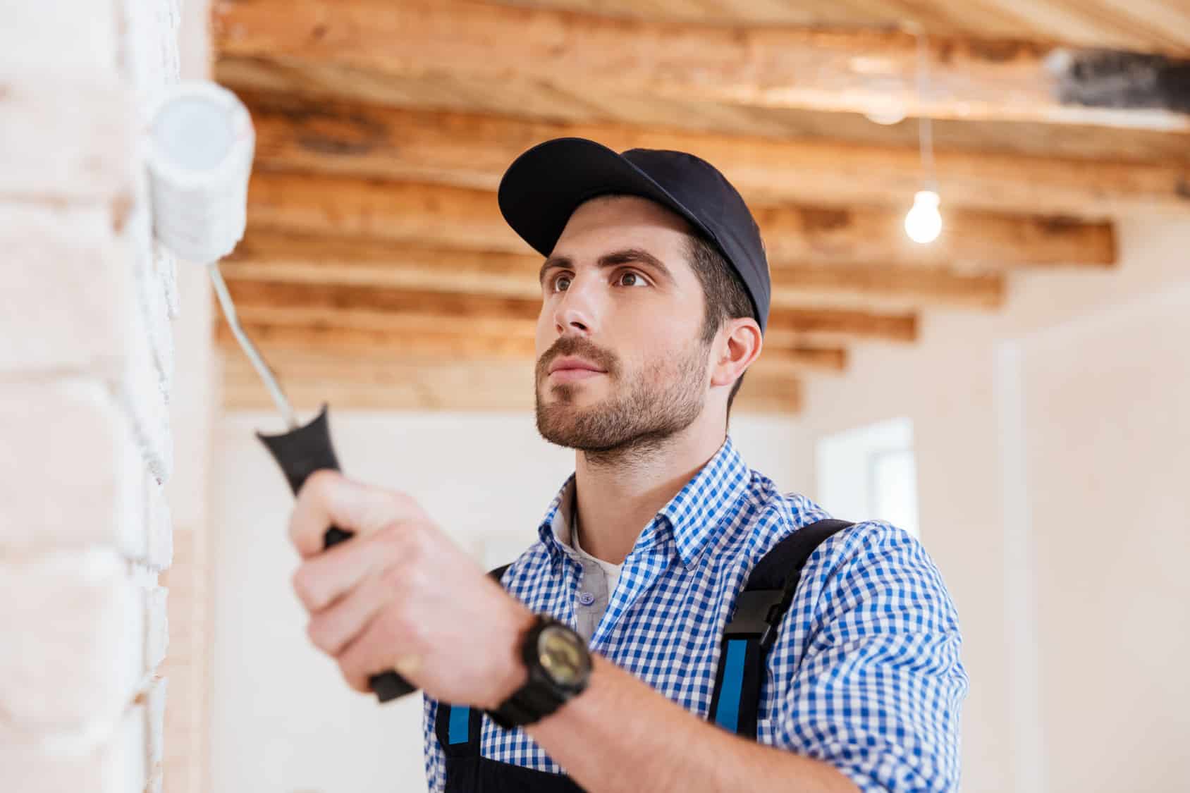Close-up portrait of a builder worker painting wall indoors