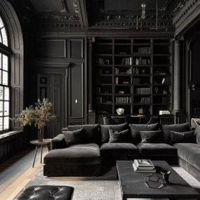 An all-black living room with paneled walls, ornate ceiling, floor-to-ceiling bookshelf, and a dark velvet sectional by an arched window.