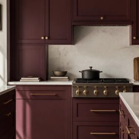 A burgundy shaker cabinet kitchen with brass hardware, marble backsplash and countertops, pro-style range, and a brass vessel sink on the island.