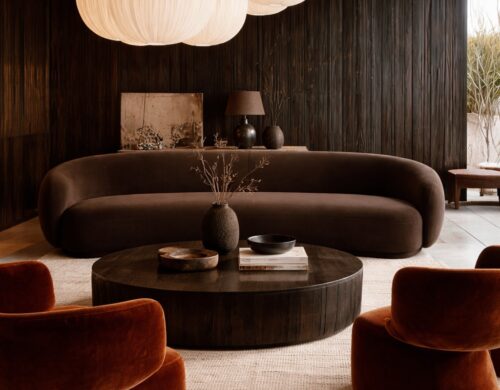 A curved brown sofa with two rust velvet chairs around a round dark wood coffee table, under cloud-shaped paper pendants against a dark wood wall.