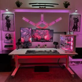 An anime-themed gaming setup with dual monitors, white keyboard, custom RGB pink lighting, clear PC tower, samurai posters, mounted katana shelf, headphones, and a mechanical keyboard on pegboard.