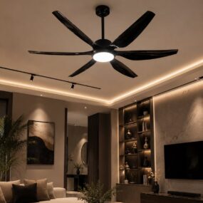 A six-blade glossy black ceiling fan with integrated light above a neutral living room with cream sectional, lit shelving, and cove lighting.