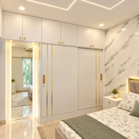 A floor-to-ceiling white sliding-door wardrobe with gold inlay and overhead storage next to a marble accent wall in a bright bedroom.