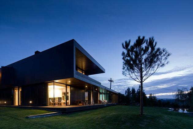 black-home-with-bright-interior-built-into-grassy-hillside-3-front-angle-evening.jpg